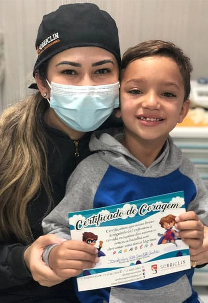 Menino com o Certificado de Coragem ao lado da dentista
