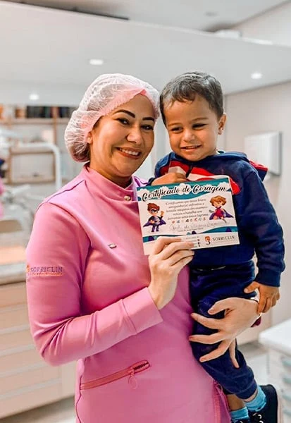 Dentista segurando um menino com o Certificado de Coragem